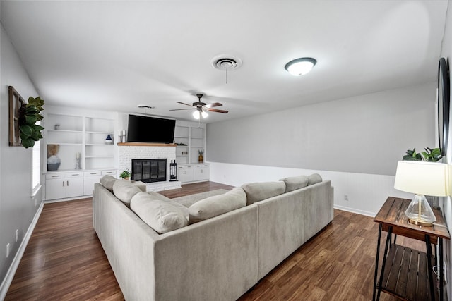 living room featuring visible vents, built in features, a ceiling fan, dark wood-type flooring, and a fireplace