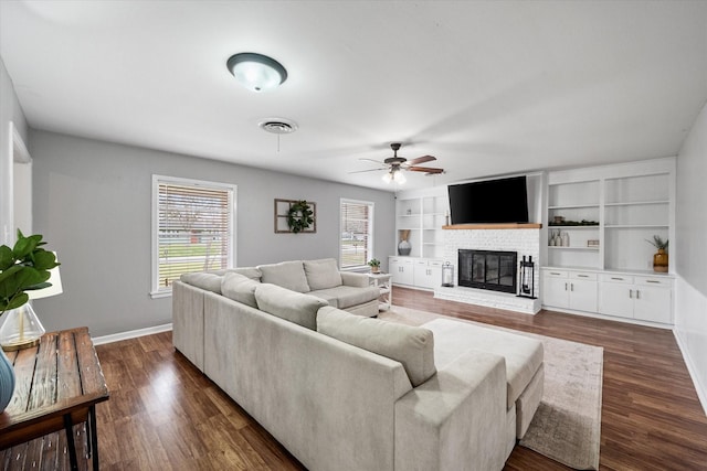 living area featuring baseboards, visible vents, dark wood-style flooring, a brick fireplace, and built in shelves