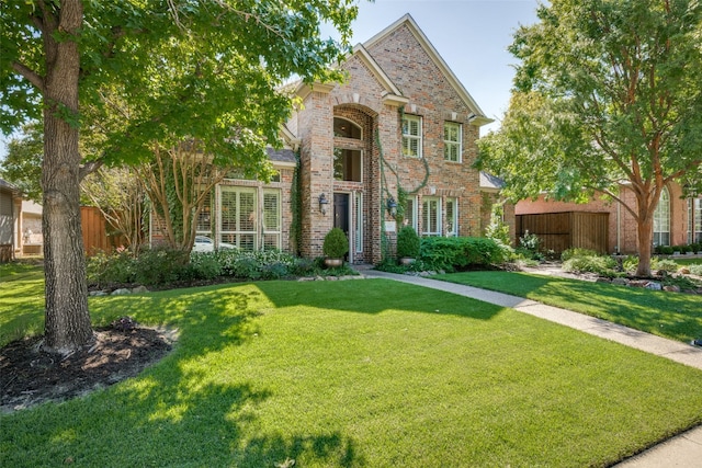 traditional home featuring a front yard, brick siding, and fence