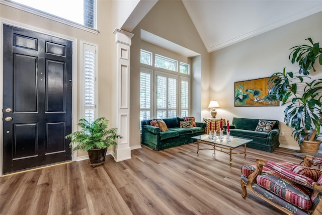 foyer entrance with ornate columns, ornamental molding, wood finished floors, high vaulted ceiling, and baseboards