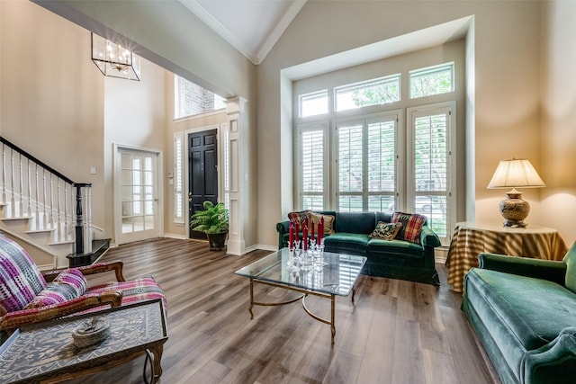 living area with baseboards, stairway, wood finished floors, crown molding, and high vaulted ceiling