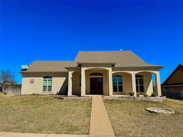 view of front of home featuring french doors, brick siding, a shingled roof, a front yard, and fence