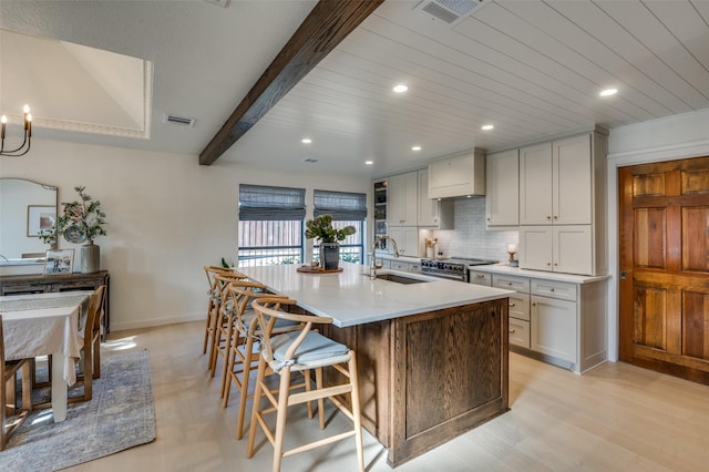 kitchen with stainless steel stove, a sink, visible vents, backsplash, and beamed ceiling