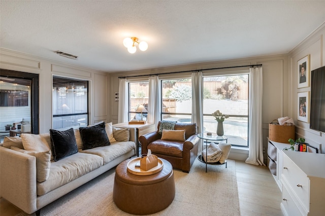 living area with light wood-style floors, visible vents, a decorative wall, and a textured ceiling