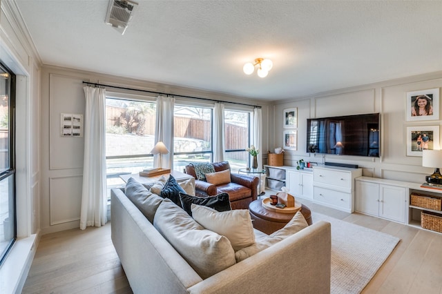 living room featuring visible vents, a decorative wall, a textured ceiling, and light wood finished floors