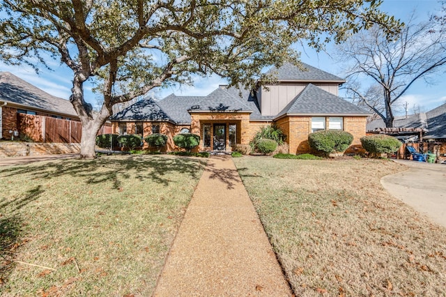 view of front of house with brick siding, fence, a front lawn, and roof with shingles