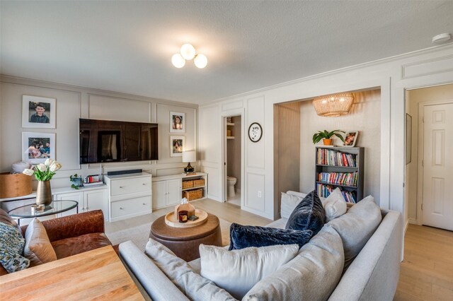 living area with light wood-type flooring, ornamental molding, and a decorative wall