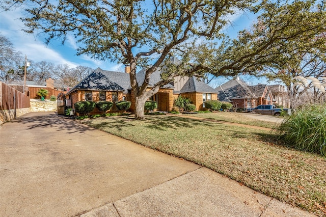 view of front of house with driveway, a chimney, fence, a front lawn, and brick siding