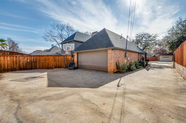 view of property exterior featuring a garage, concrete driveway, roof with shingles, fence, and brick siding