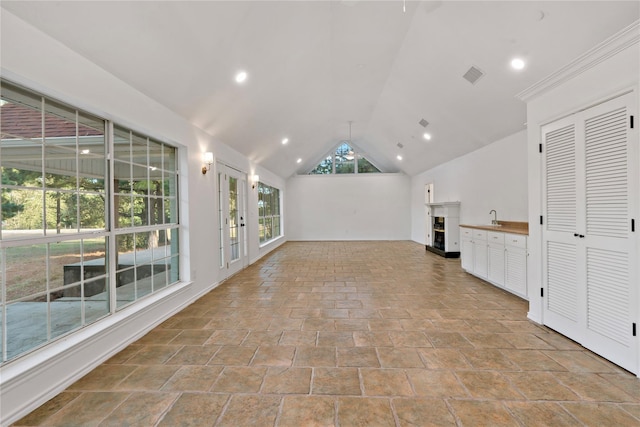 unfurnished living room with a fireplace with raised hearth, lofted ceiling, recessed lighting, a sink, and visible vents