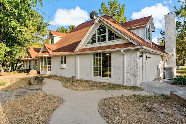 back of house featuring central AC, brick siding, and a chimney