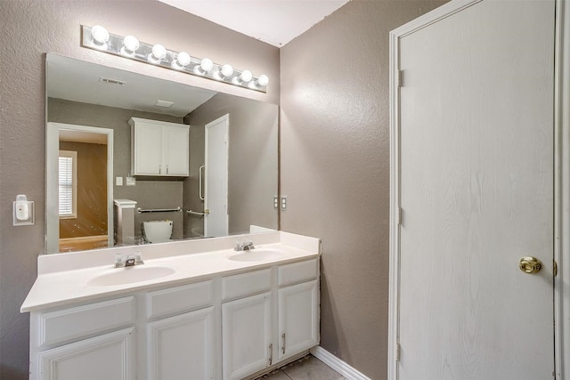 bathroom featuring a textured wall, double vanity, a sink, and visible vents