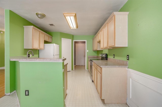 kitchen featuring visible vents, light brown cabinetry, freestanding refrigerator, and stainless steel range with electric cooktop