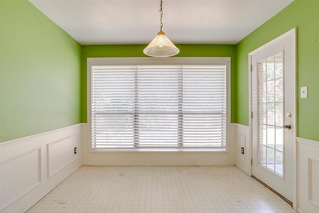 unfurnished dining area featuring tile patterned floors, a decorative wall, and wainscoting