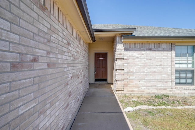 entrance to property featuring roof with shingles and brick siding