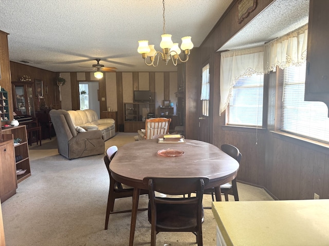 dining area featuring light carpet, wood walls, and a textured ceiling