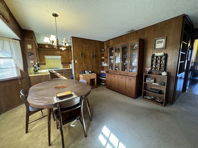 dining area featuring a textured ceiling, wooden walls, an inviting chandelier, and light colored carpet