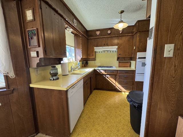 kitchen featuring white appliances, light floors, a textured ceiling, under cabinet range hood, and a sink