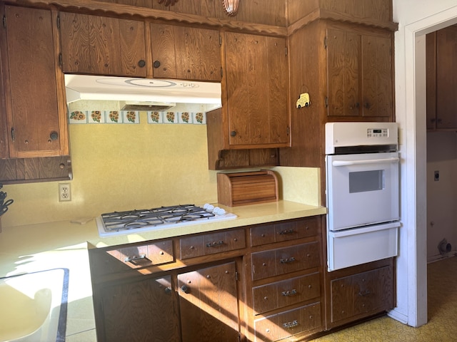 kitchen featuring white appliances, under cabinet range hood, light countertops, and a warming drawer