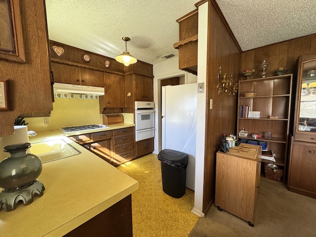 kitchen featuring white appliances, wooden walls, a textured ceiling, under cabinet range hood, and a warming drawer