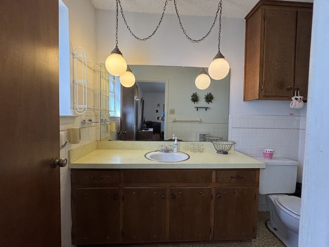 half bath with a wainscoted wall, tile walls, toilet, vanity, and a textured ceiling