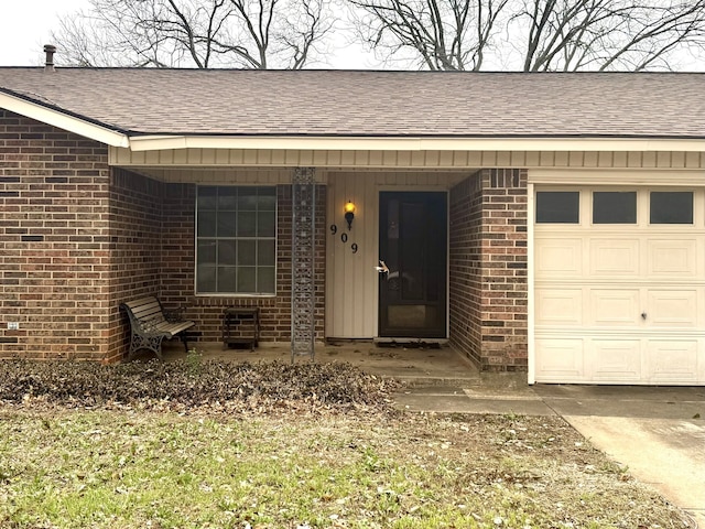 property entrance featuring a shingled roof, an attached garage, and brick siding