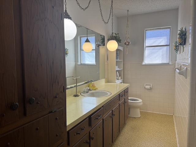 bathroom with a healthy amount of sunlight, toilet, a textured ceiling, and wainscoting