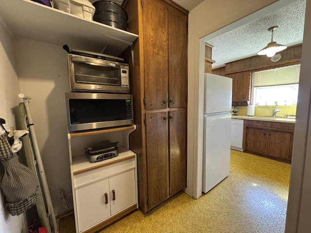 kitchen with white appliances, light countertops, a textured ceiling, light floors, and a sink