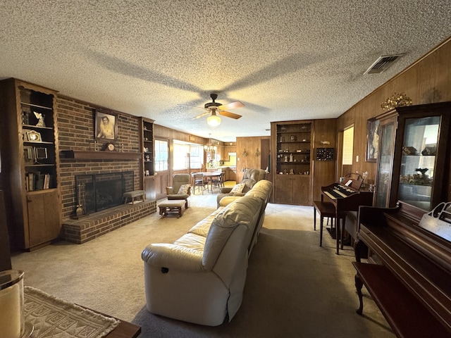 living room featuring wooden walls, visible vents, a textured ceiling, carpet floors, and a brick fireplace