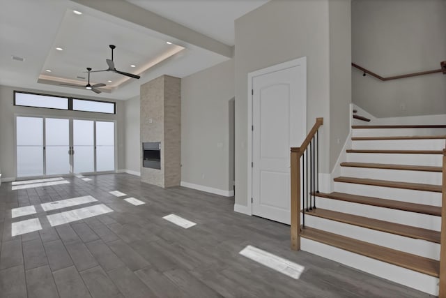 unfurnished living room with baseboards, a raised ceiling, a tile fireplace, stairway, and dark wood-type flooring