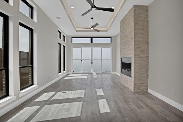 unfurnished living room with wood finished floors, a fireplace, a raised ceiling, and baseboards