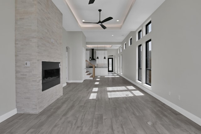 unfurnished living room featuring a large fireplace, baseboards, a tray ceiling, and wood finished floors