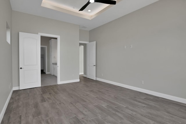 unfurnished bedroom with dark wood-type flooring, a raised ceiling, and baseboards