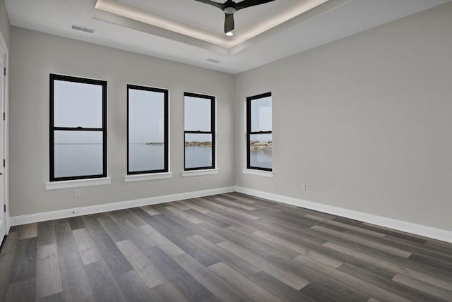 empty room featuring dark wood-style floors, visible vents, baseboards, and a raised ceiling