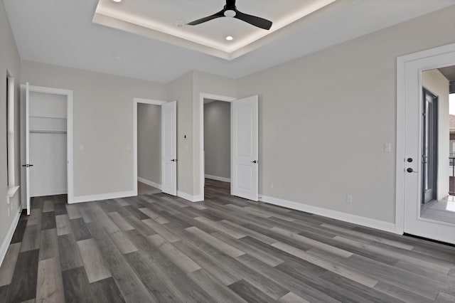 unfurnished bedroom featuring dark wood-style flooring, a raised ceiling, ceiling fan, and baseboards