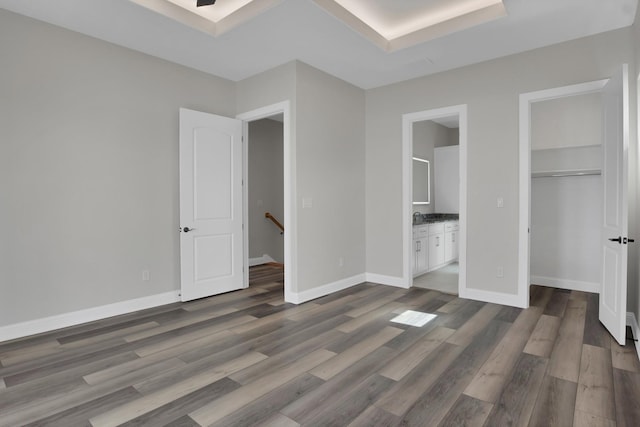 unfurnished bedroom featuring dark wood-type flooring, a closet, connected bathroom, and baseboards