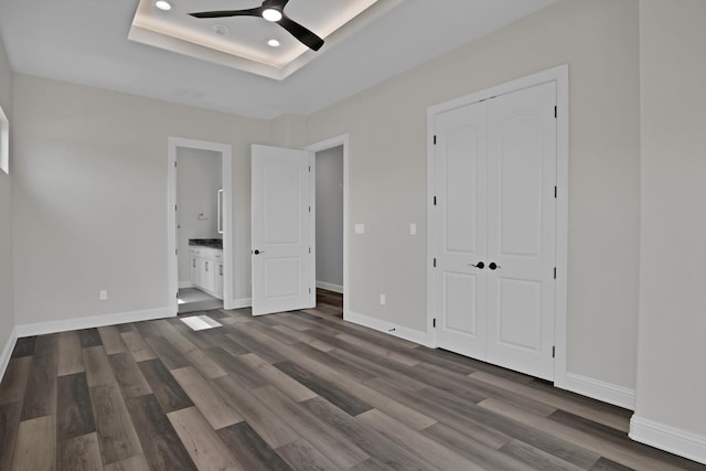 unfurnished bedroom featuring a raised ceiling, dark wood finished floors, and baseboards