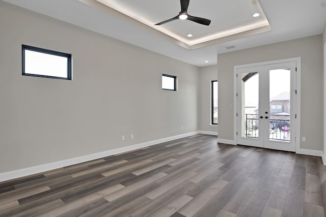 empty room featuring a tray ceiling, french doors, dark wood-style flooring, recessed lighting, and baseboards