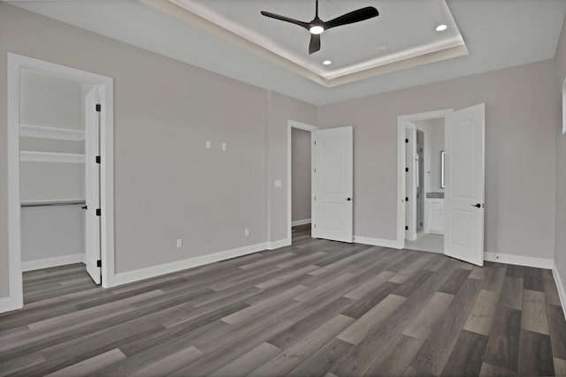 unfurnished bedroom featuring baseboards, dark wood finished floors, connected bathroom, a raised ceiling, and recessed lighting