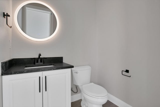 half bathroom featuring toilet, vanity, and baseboards