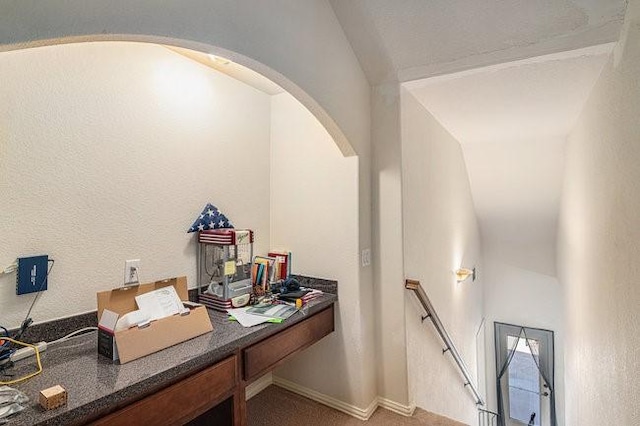 office featuring light carpet, arched walkways, and a textured wall