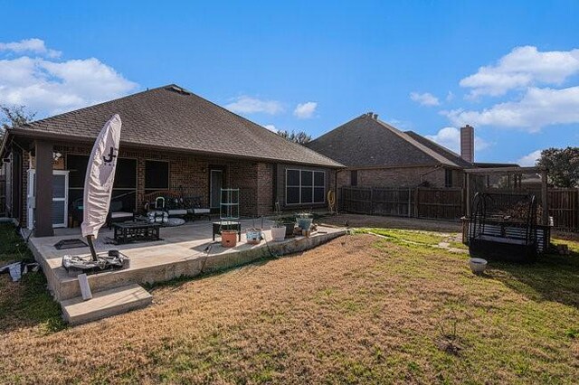 back of property featuring a shingled roof, a patio, fence, a yard, and brick siding