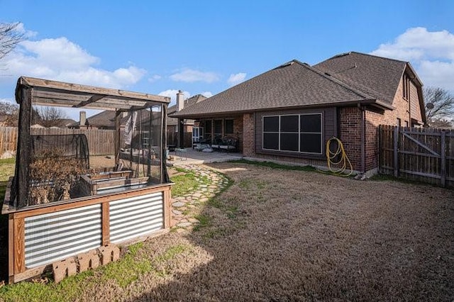 back of property with a patio, brick siding, a fenced backyard, and a vegetable garden