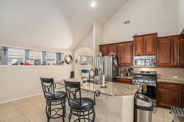 kitchen with a center island with sink, a breakfast bar, light stone countertops, stainless steel appliances, and a sink