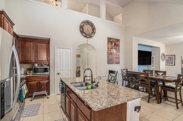 kitchen featuring arched walkways, light tile patterned floors, a kitchen island with sink, stainless steel appliances, and a sink