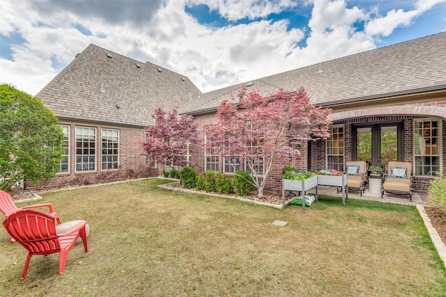 back of house featuring a shingled roof, a lawn, a patio, and brick siding