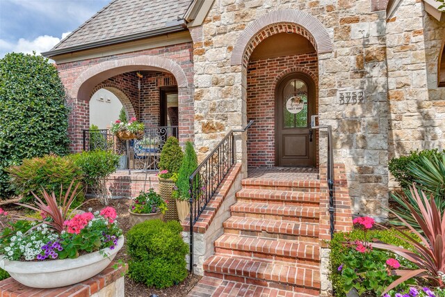 property entrance featuring stone siding, brick siding, and roof with shingles