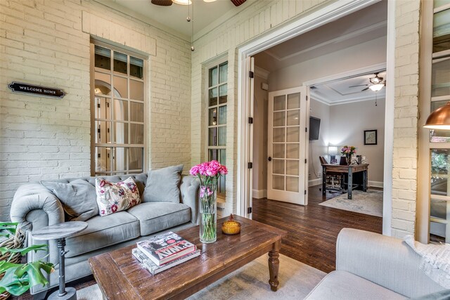 living room with ceiling fan, brick wall, wood finished floors, baseboards, and crown molding