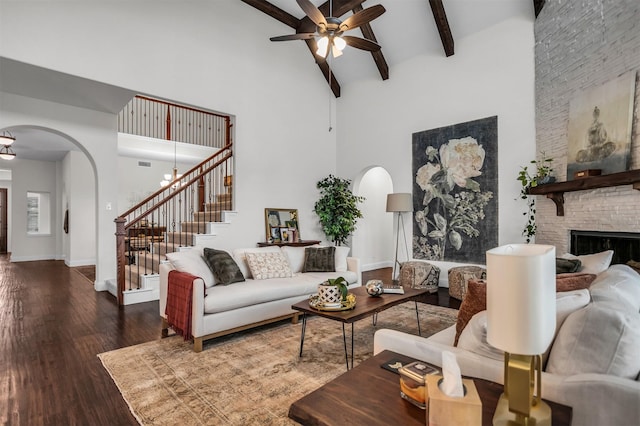 living room featuring arched walkways, stairway, wood finished floors, beamed ceiling, and a high ceiling