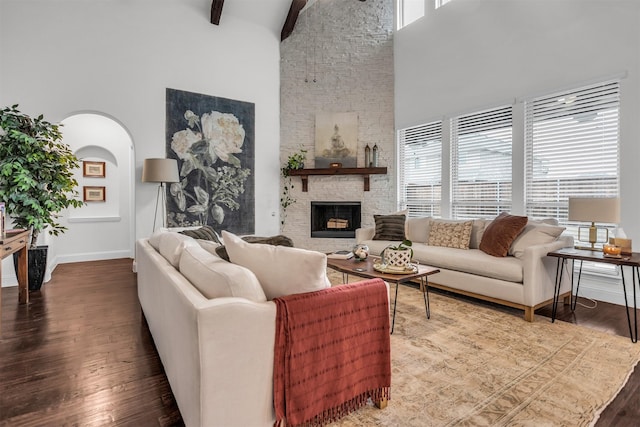 living area with a high ceiling, a fireplace, wood finished floors, baseboards, and beam ceiling